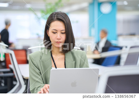 A smiling foreign businesswoman working on her laptop in a brightly lit office. 138656367