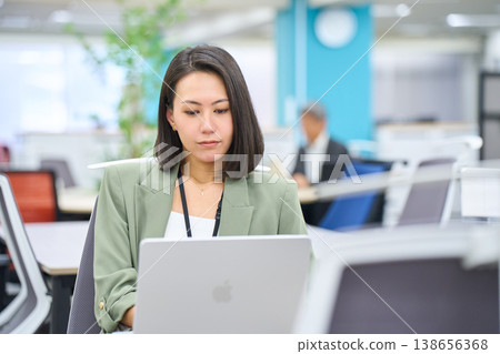 A smiling foreign businesswoman working on her laptop in a brightly lit office. A smiling foreign businesswoman working on her laptop in a brightly lit office. 138656368