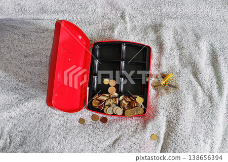 Open red cash box on textile bed blanket with scattered coins Open red cash box on textile bed blanket with scattered coins 138656394
