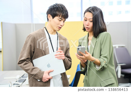 一家外國公司的年輕男女在辦公室對著鏡頭微笑,手裡拿著他們的設備。 一家外國公司的年輕男女在辦公室對著鏡頭微笑,手裡拿著他們的設備。 138656413