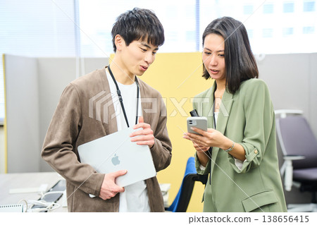 Young men and women from a foreign company smile at the camera in their office, holding their devices. Young men and women from a foreign company smile at the camera in their office, holding their devices. 138656415