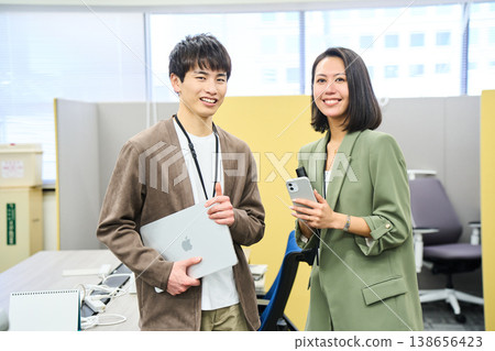Young men and women from a foreign company smile at the camera in their office, holding their devices. Young men and women from a foreign company smile at the camera in their office, holding their devices. 138656423