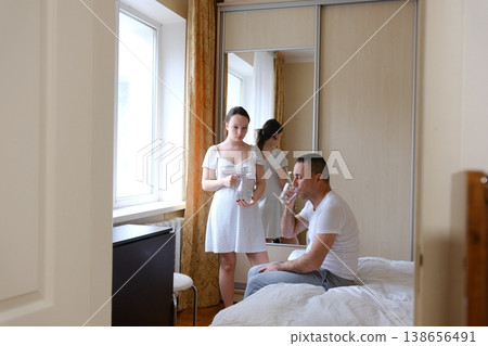 Teenage daughter pouring water for father at home cozy beige bedroom caring family moment weekend routine indoor lifestyle Teenage daughter pouring water for father at home cozy beige bedroom caring family moment weekend routine indoor lifestyle 138656491