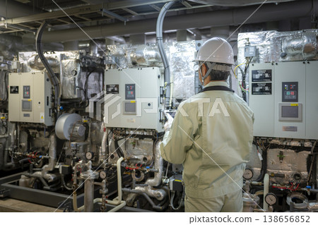 A worker inspecting the building's air conditioning system (absorption chiller/heater) from behind. (Image of building maintenance staff) A worker inspecting the building's air conditioning system (absorption chiller/heater) from behind. (Image of building maintenance staff) 138656852