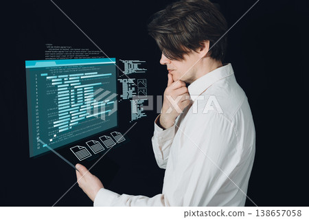 A white-shirted engineer/programmer ponders as he looks at the holographic code and data screens appearing on his tablet. A white-shirted engineer/programmer ponders as he looks at the holographic code and data screens appearing on his tablet. 138657058