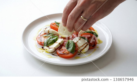 Preparing caprese salad: hand adding mozzarella to tomatoes and basil leaves with balsamic glaze food styling olive oil tomatoes mozzarella preparing balsamic appetizer vegetarian restaurant 138657946