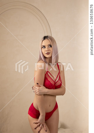 Confident woman in red lace lingerie posing against wall 138658676