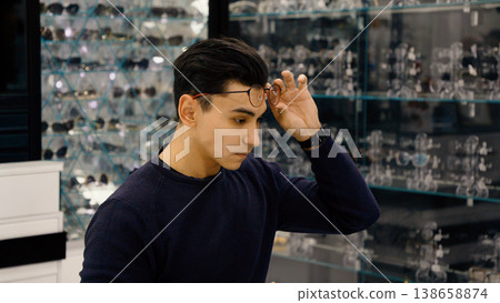 Young man trying on new glasses in eyewear store Young man trying on new glasses in eyewear store 138658874