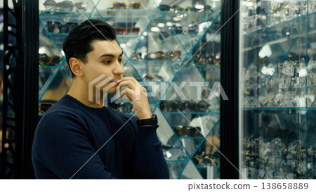Thoughtful man in eyewear store touching his face 138658889