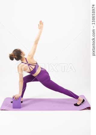 Fit woman in purple outfit using a block for yoga stretching Fit woman in purple outfit using a block for yoga stretching 138658974