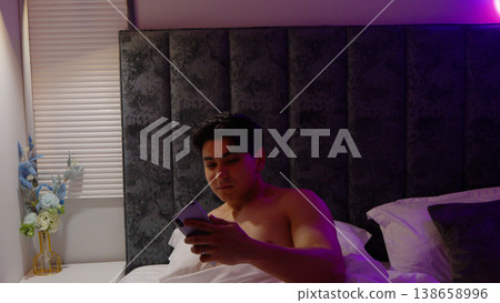 Young man using smartphone while lying in bed at night time Young man using smartphone while lying in bed at night time 138658996