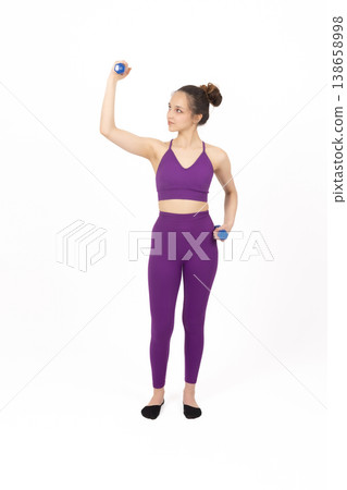 Athletic woman in purple outfit exercising with dumbbell in studio Athletic woman in purple outfit exercising with dumbbell in studio 138658998