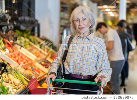 Elderly woman with shopping cart chooses groceries 138659873