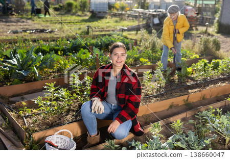 Smiling young female farmer posing with basket and garden instruments during season of sowing on sunny day of autumn 138660047