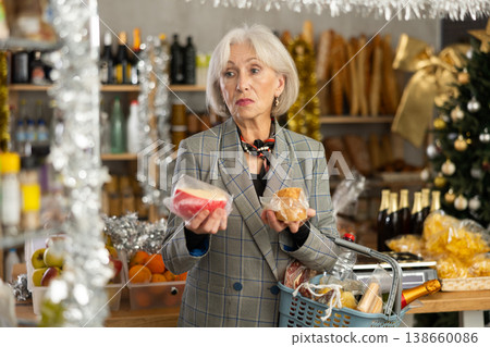 Elderly woman examines cheese in store on eve of New Year holidays Elderly woman examines cheese in store on eve of New Year holidays 138660086