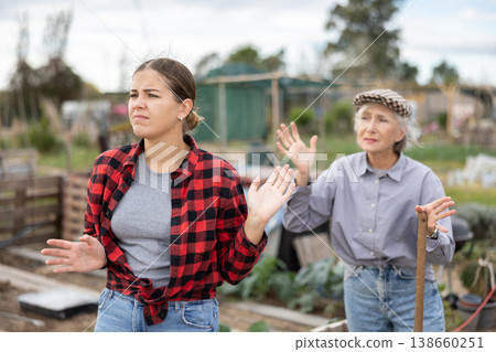 Two angry casual women neighbors of different ages arguing during the vegetable garden season on sunny day of spring Two angry casual women neighbors of different ages arguing during the vegetable garden season on sunny day of spring 138660251