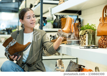 Girl buyer looks at footwear from new collection and picks up new pair of boots for winter. Girl buyer looks at footwear from new collection and picks up new pair of boots for winter. 138660300