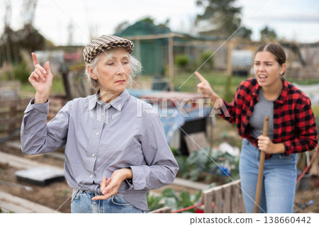 Two upset young and old female neighbors disagree with each other while digging garden on smallholding in autumn 138660442