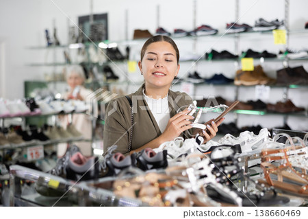 Girl client is demanding to inspect sandals in shoe showroom Girl client is demanding to inspect sandals in shoe showroom 138660469