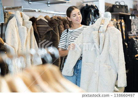 Young girl choosing white fur coat in clothing shop Young girl choosing white fur coat in clothing shop 138660497