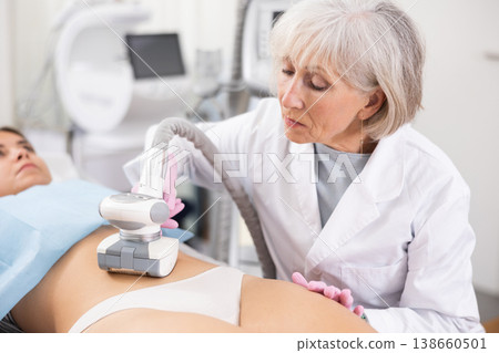 Young woman getting ultrasound cavitation body contouring treatment, anti-cellulite therapy, vacuum massage from old female cosmetologist. Hardware cosmetology for body sculpting 138660501