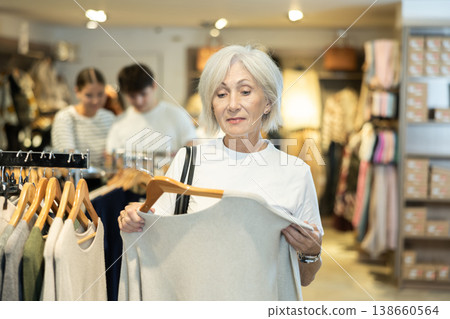 elderly lady carefully examines selection of sweaters elderly lady carefully examines selection of sweaters 138660564