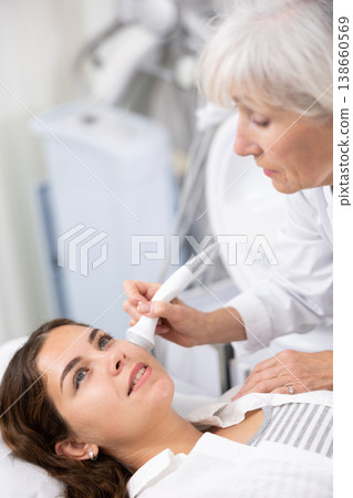 Young female visitor receiving hardware electric lifting massage with help of old female beautician in spa salon indoors 138660569