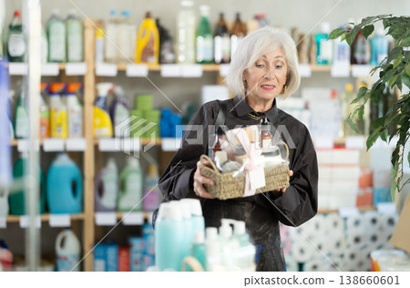 Elderly woman chooses gift set of shampoo, liquid soap and cosmetic items in supermarket 138660601