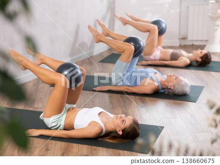 Family grandmother, mother and granddaughter perform fitness exercises lying on floor with softball. Family grandmother, mother and granddaughter perform fitness exercises lying on floor with softball. 138660675