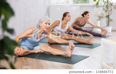 Yoga class of sports women performing Head to Knee Forward Bend Pose, or Janu Sirsasana after practicing together Yoga class of sports women performing Head to Knee Forward Bend Pose, or Janu Sirsasana after practicing together 138660731
