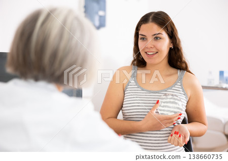 Faceless elderly female doctor showing breast silicone implant for breast augmentation for young woman during consultation in beauty clinic 138660735