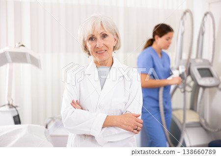 Smiling old woman doctor posing against background of cosmetology devices Smiling old woman doctor posing against background of cosmetology devices 138660789