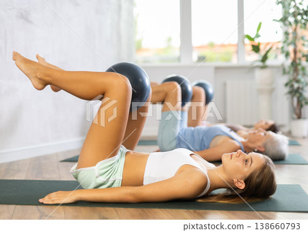 Family grandmother, mother and granddaughter perform fitness exercises lying on floor with softball. Family grandmother, mother and granddaughter perform fitness exercises lying on floor with softball. 138660793