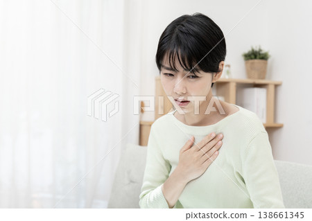 A woman clutches her chest, suddenly feeling unwell; chest pain, stress. A woman clutches her chest, suddenly feeling unwell; chest pain, stress. 138661345