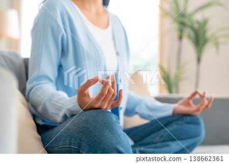Happy young Asian woman practicing yoga and meditation at home sitting on couch Happy young Asian woman practicing yoga and meditation at home sitting on couch 138662361