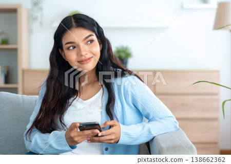 Smiling pretty young Asian woman sitting on cozy couch Smiling pretty young Asian woman sitting on cozy couch 138662362