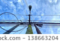 Tangled Utility Poles and Power Lines Against Blue Sky. A low-angle shot of weathered utility poles covered in moss with a complex network of electrical wires against a bright blue sky with light clou 138663204
