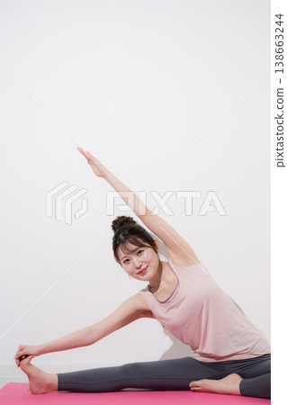 A woman stretching her side while doing a split, a yoga image for improving flexibility, full body view, looking directly at the camera. A woman stretching her side while doing a split, a yoga image for improving flexibility, full body view, looking directly at the camera. 138663244