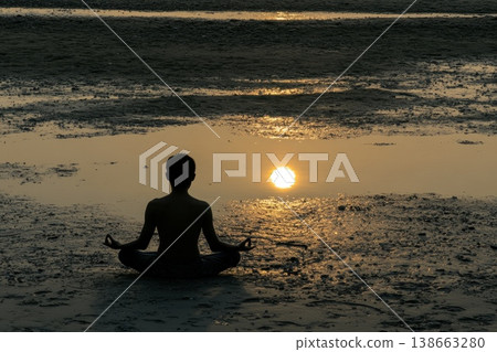 Serene Silhouette of Person Meditating on a Shoreline During Golden Sunset Reflection Serene Silhouette of Person Meditating on a Shoreline During Golden Sunset Reflection 138663280