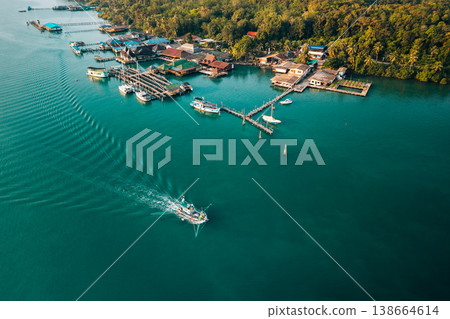 Aerial view of a traditional fishing village with a moving boat and clear emerald water. Aerial view of a traditional fishing village with a moving boat and clear emerald water. 138664614