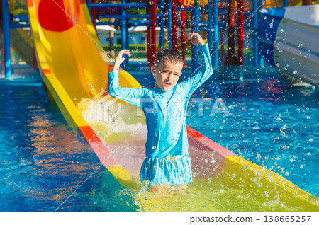 Cute happy child boy enjoys and has fun at water park in summer on vacation. Children's aqua park with water slide and swimming pool in resort Cute happy child boy enjoys and has fun at water park in summer on vacation. Children's aqua park with water slide and swimming pool in resort 138665257