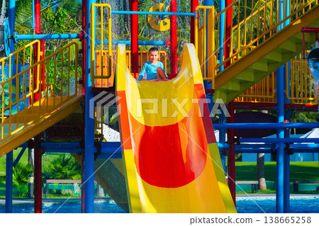 Caucasian happy child boy enjoys and has fun at water park in summer on vacation. Children's aquapark with water slide and swimming pool in resort Caucasian happy child boy enjoys and has fun at water park in summer on vacation. Children's aquapark with water slide and swimming pool in resort 138665258