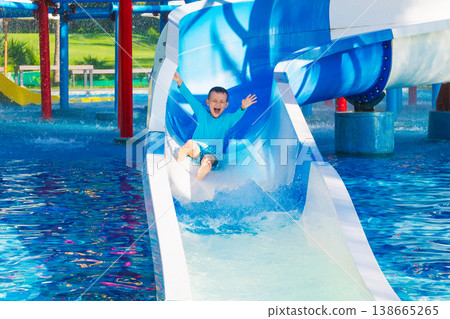 happy funny child boy rides a water slide in water park in summer vacation. Children's aqua park in swimming pool at resort 138665265