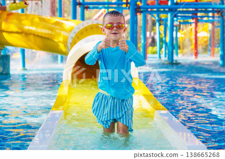 Cute happy kid boy enjoys and has fun at water park in summer on vacation. Children's aquapark with water slide and swimming pool Cute happy kid boy enjoys and has fun at water park in summer on vacation. Children's aquapark with water slide and swimming pool 138665268