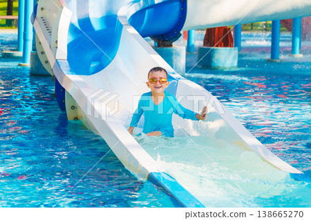 happy cute child boy rides a water slide in a water park in summer vacation. Children's aquapark in swimming pool at resort happy cute child boy rides a water slide in a water park in summer vacation. Children's aquapark in swimming pool at resort 138665270