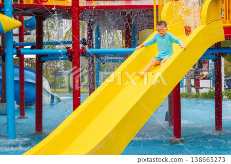 Caucasian cute child boy rides a water slide in water park in summer vacation. Children's aquapark in swimming pool at the resort 138665273
