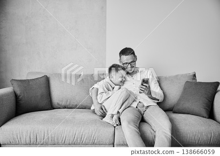 Cute moment of dad and little kid. Father showing son funny videos. Handsome man and his son laughing at funny picture. Black and white image. Cute moment of dad and little kid. Father showing son funny videos. Handsome man and his son laughing at funny picture. Black and white image. 138666059