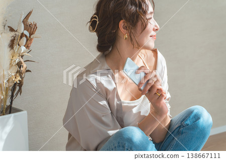 A woman's profile as she sits on the floor and looks at her smartphone. A woman's profile as she sits on the floor and looks at her smartphone. 138667111