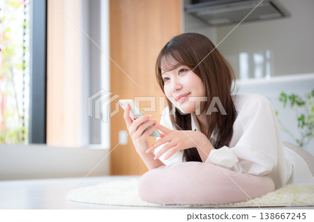一位女士在家中放鬆,面朝下躺著,看著她的智慧型手機。 一位女士在家中放鬆,面朝下躺著,看著她的智慧型手機。 138667245