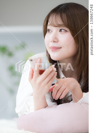 一張輕鬆的日常照片,照片中一位女性面朝下躺在家中,看著她的智慧型手機。 一張輕鬆的日常照片,照片中一位女性面朝下躺在家中,看著她的智慧型手機。 138667248